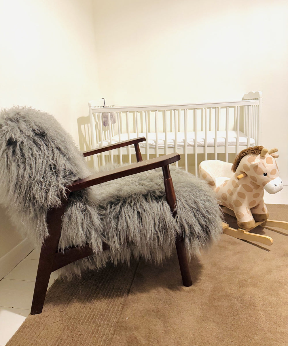 Grey Mongolian fur accent chair with walnut frame beside a cot in a real nursery, side view