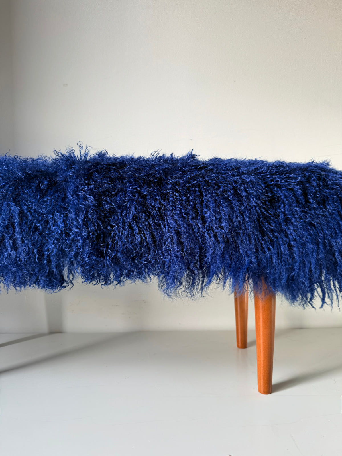 Handmade royal blue Mongolian fur single bench on solid wood tapered legs, photographed in our London studio