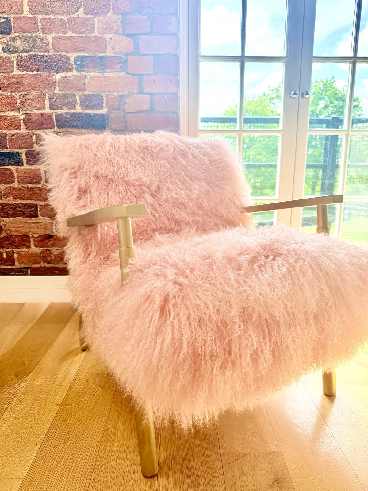 Handmade blush pink Mongolian fur accent chair with gold frame against exposed brick in our studio