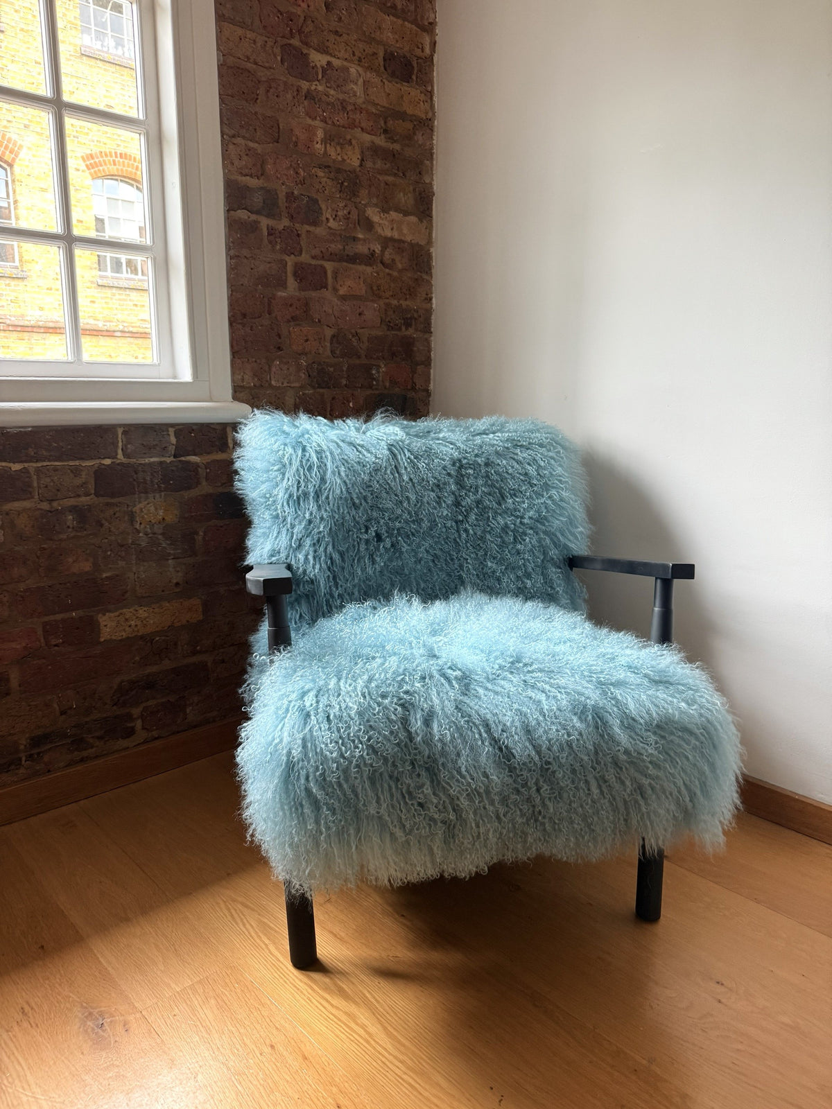 Handmade duck egg blue Mongolian fur accent chair with matt black frame against exposed brick in our London studio