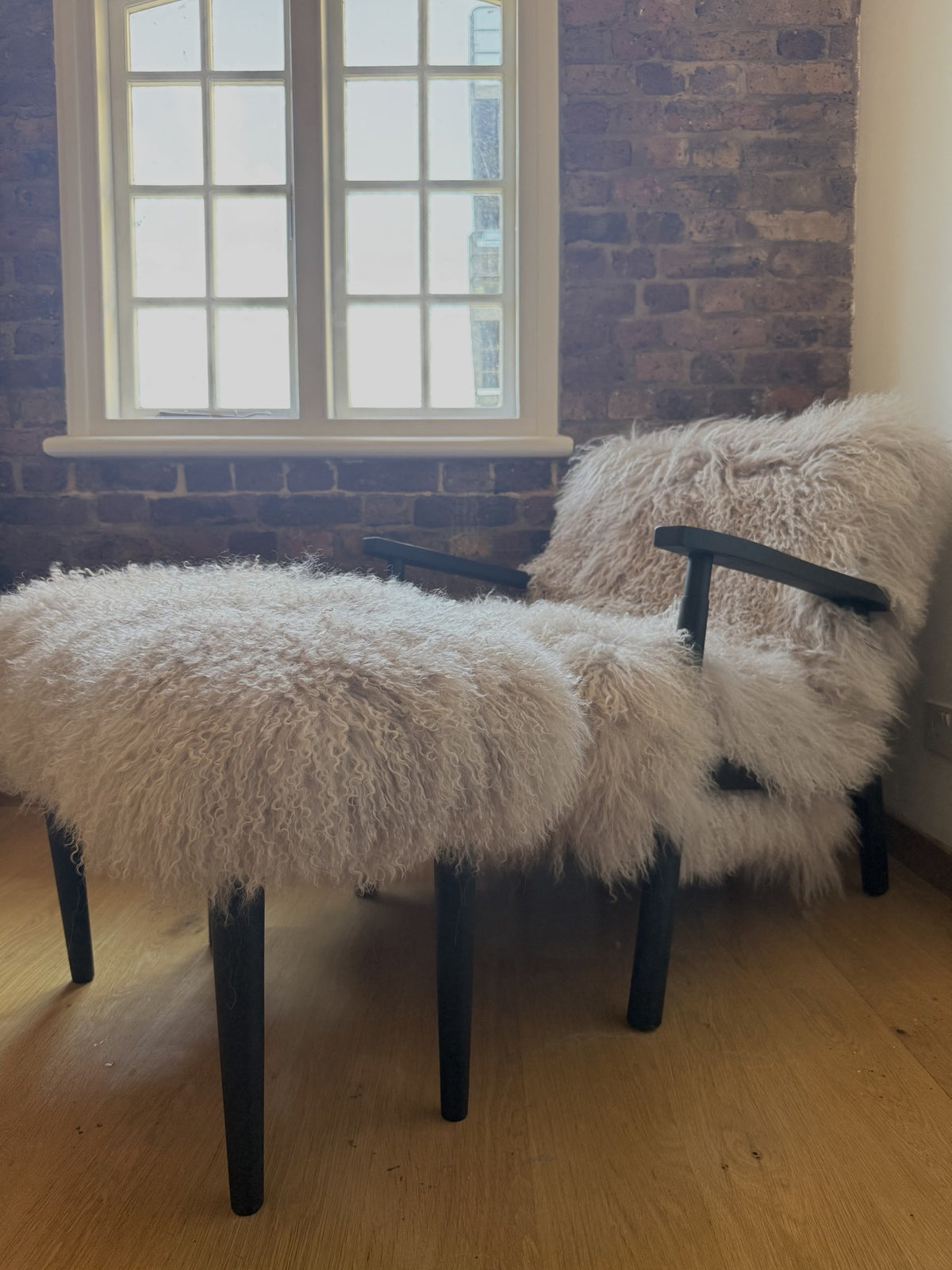 Oyster Mongolian fur chair and matching footstool on matt black frames, by a sash window