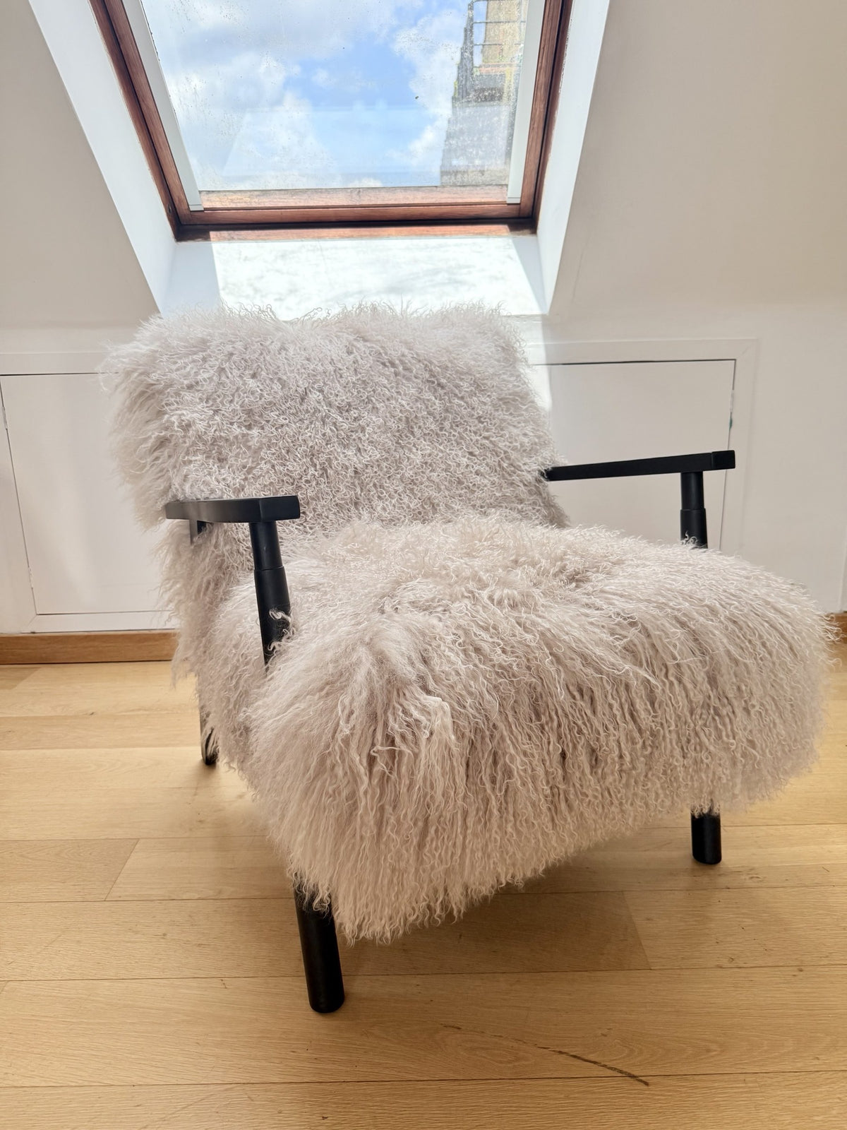Handmade oyster Mongolian fur accent chair with matt black frame beneath a skylight