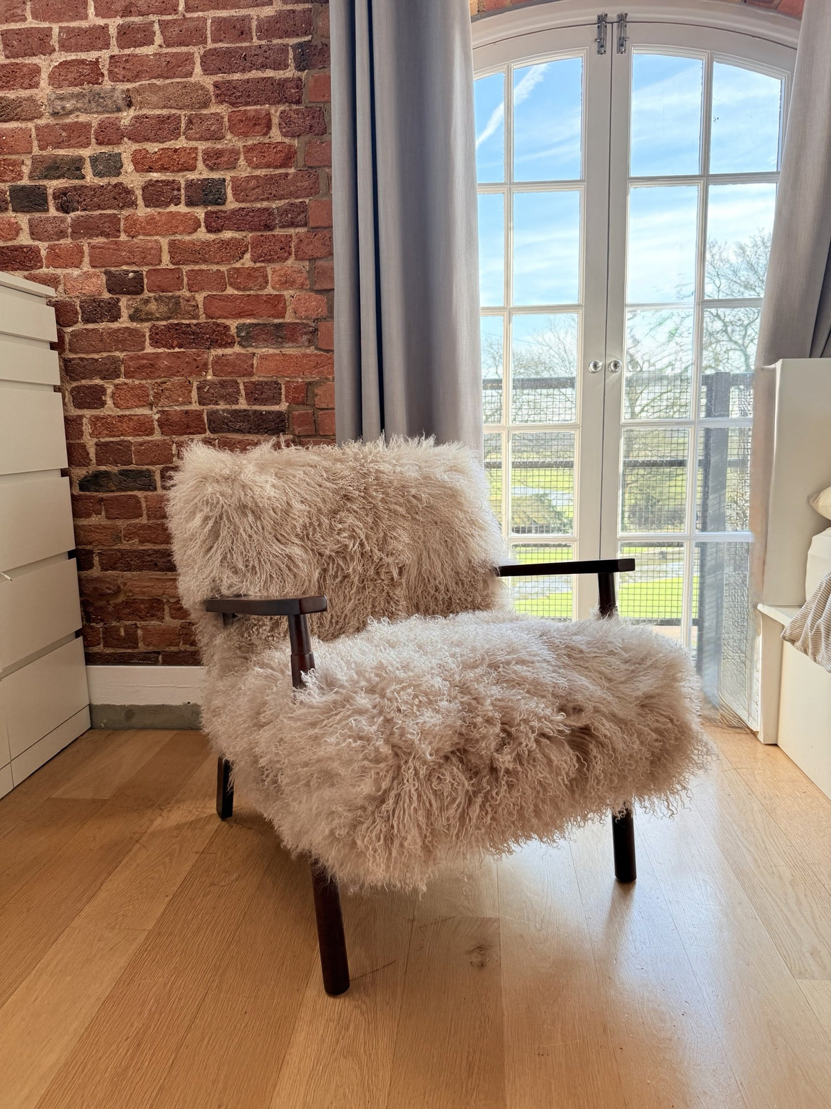 Handmade oyster Mongolian fur accent chair with curved walnut arms by an arched window in our London studio