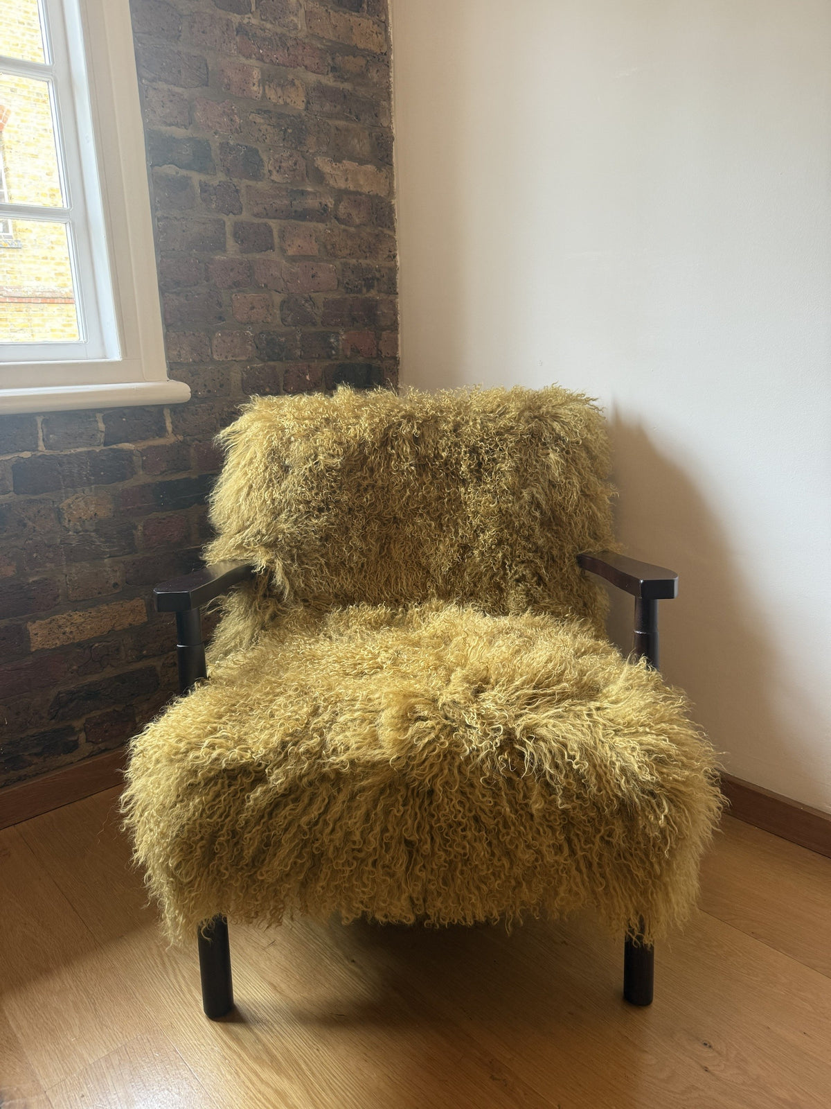 Handmade sandstorm Mongolian fur accent chair with dark walnut frame against exposed brick in our London studio