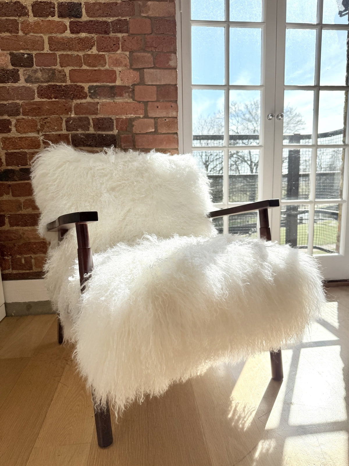 Handmade white Mongolian fur accent chair with curved walnut arms in front of tall French windows